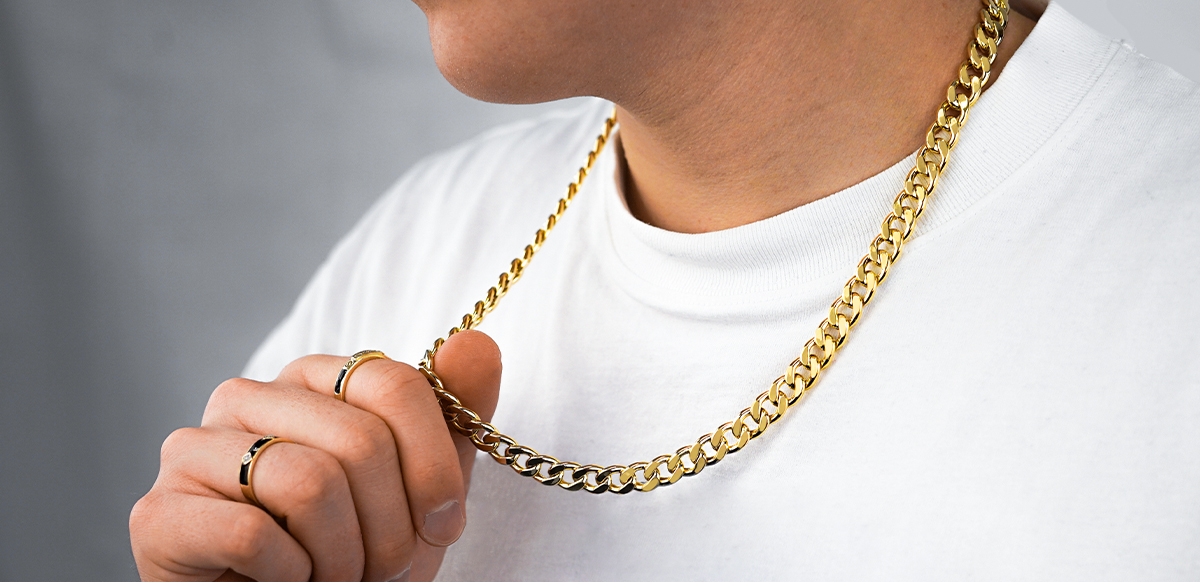Ein Mann mit zwei gold-schwarzen Ringen, der seine dicke Goldkette um den Hals hält